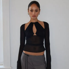 Woman wearing a black long-sleeve top with cut-out design and gray pants against a white wall.