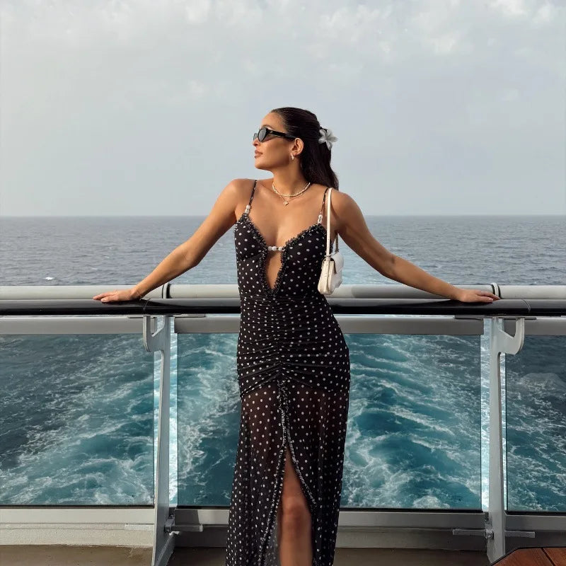 Woman in a black polka dot dress standing on a cruise ship deck with ocean view