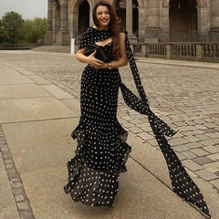 Woman in a black polka dot dress holding a matching clutch in an outdoor setting.