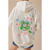 Beige hoodie with colorful floral and heart designs on the back, worn by a person.
