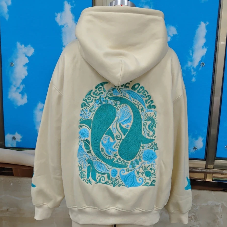 Beige hoodie with blue ocean-themed design on the back against a blue sky background