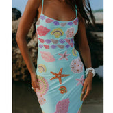 Woman wearing a blue dress with colorful shell and starfish patterns on a beach.
