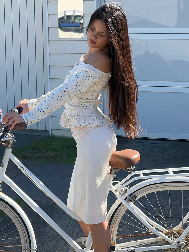 Woman in a white dress standing next to a white bicycle outdoors.