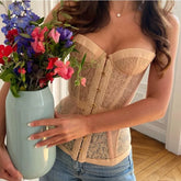 Woman holding a vase of flowers wearing a beige lace corset.