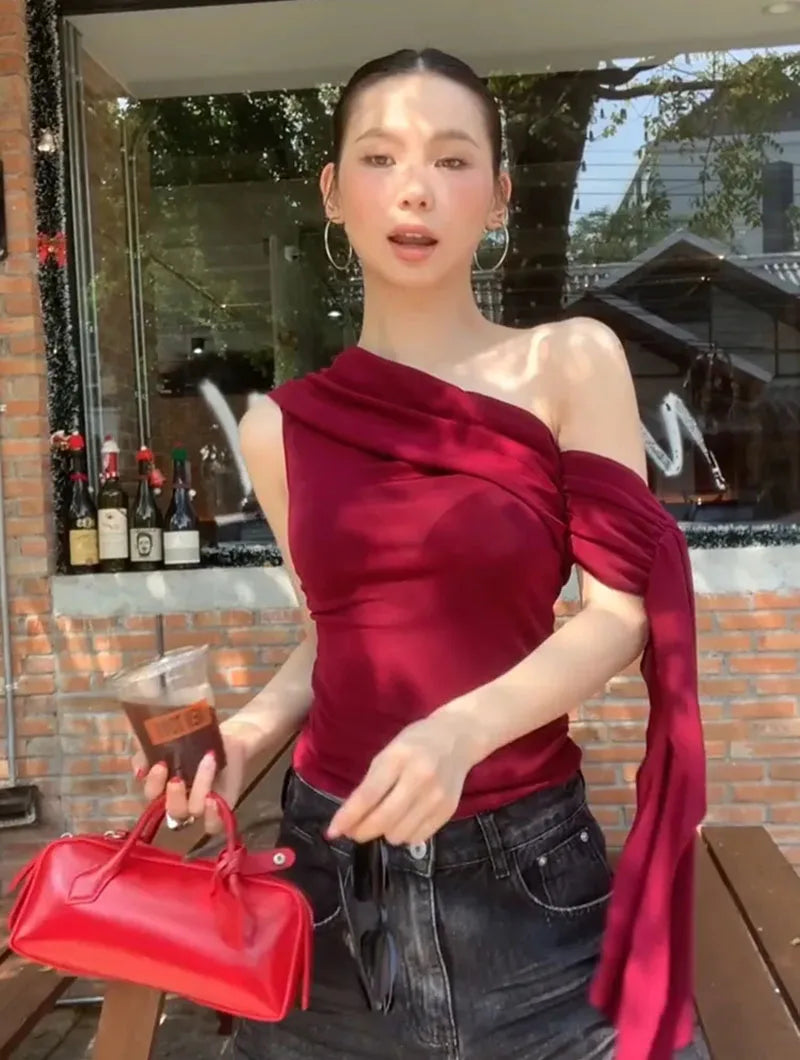 Woman in a red top holding a red handbag outdoors.