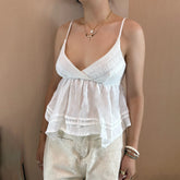 Woman wearing a white lace top and light-colored pants against a beige background