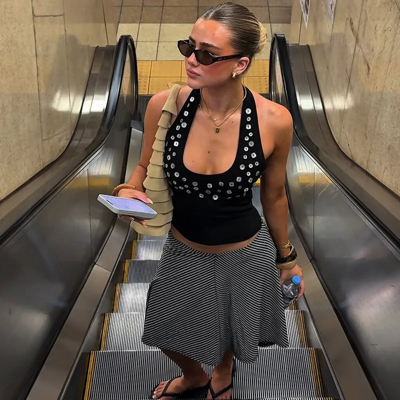 Woman descending an escalator wearing a black top with sequins and a striped skirt.