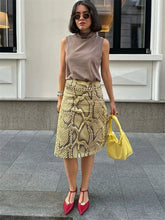 Woman wearing a patterned skirt and sleeveless top, holding a yellow handbag on a city street.