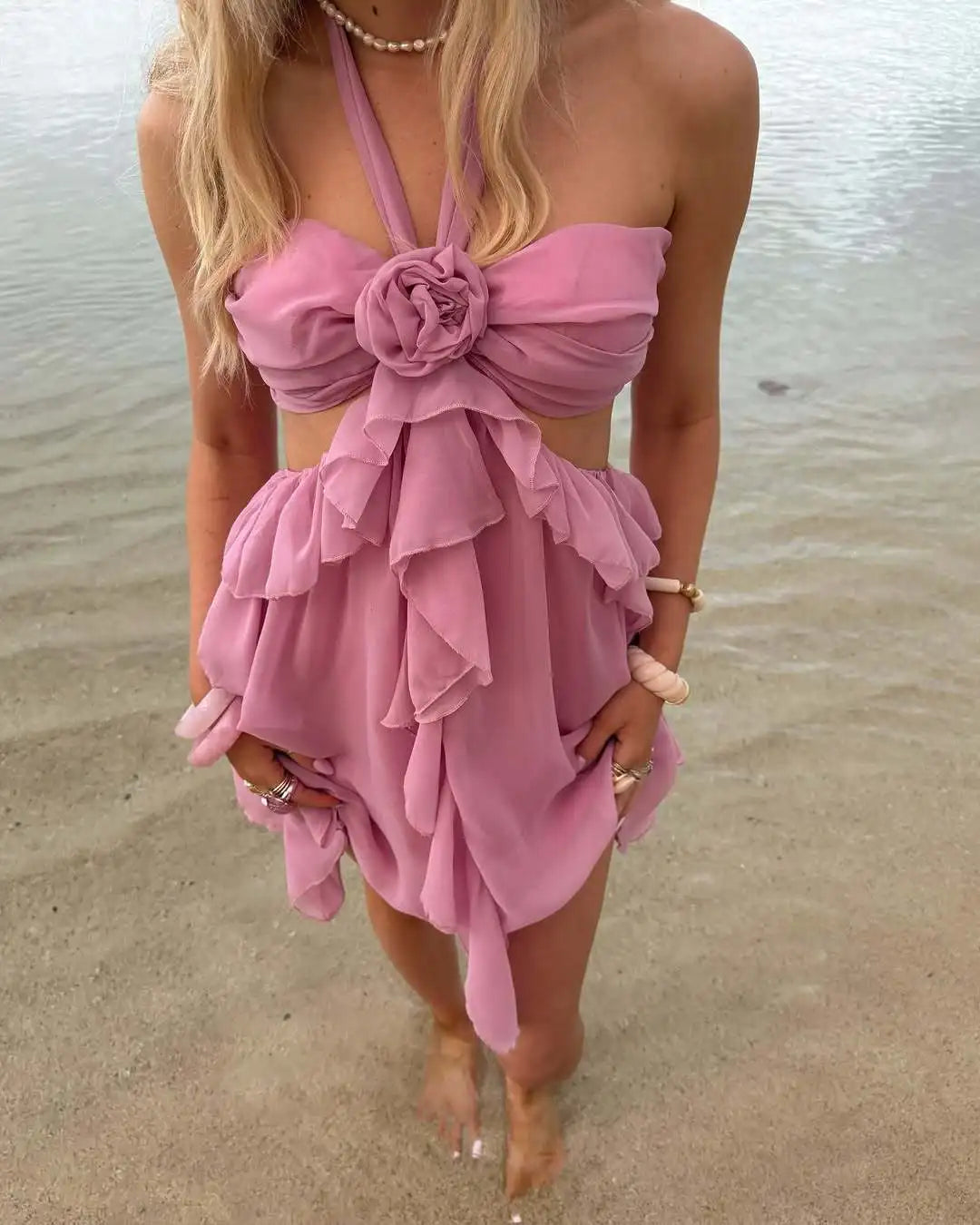 Woman wearing a pink dress with floral details on a beach.