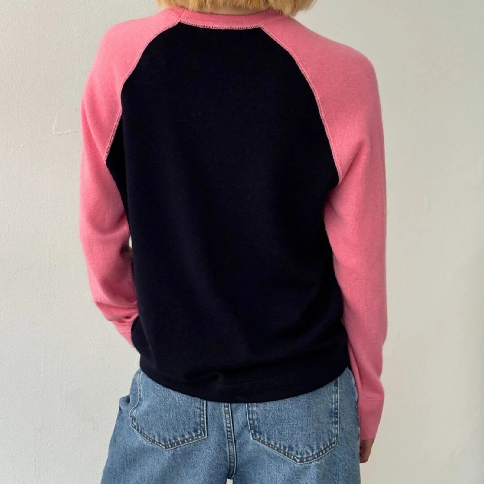 Person wearing a pink and black baseball-style sweatshirt with blue jeans