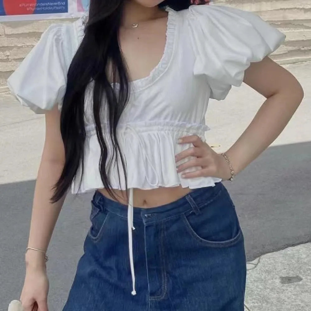 Person wearing a white top and blue jeans standing outdoors.