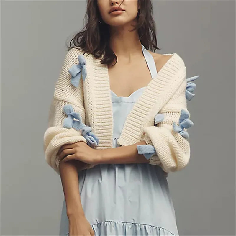 Woman wearing a cream cardigan with blue floral details on a gray background