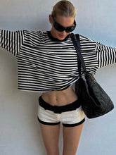 Person wearing a black and white striped sweater and shorts with a black handbag against a light background