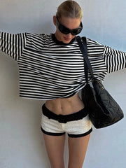Person wearing a black and white striped sweater and shorts with a black handbag against a light background