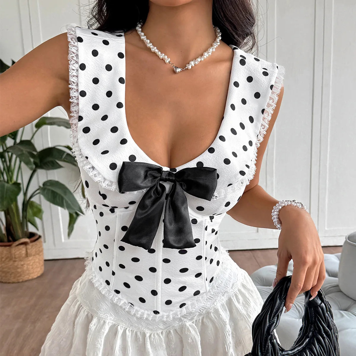 Woman wearing a white polka dot dress with a black bow in a room setting.