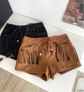 Brown suede shorts with fringe details on a white surface, next to a black box and sunglasses.