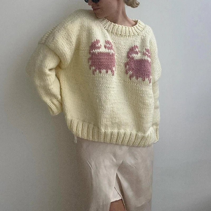 Person wearing a light yellow knitted sweater with pink ghost designs against a plain background