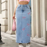Person wearing a blue denim skirt with pink bows and a pink top, standing in front of classical architecture.
