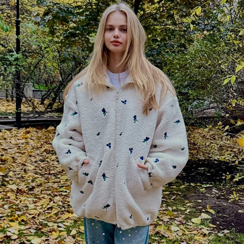 Woman wearing a patterned beige jacket in an autumn setting with fallen leaves and trees.