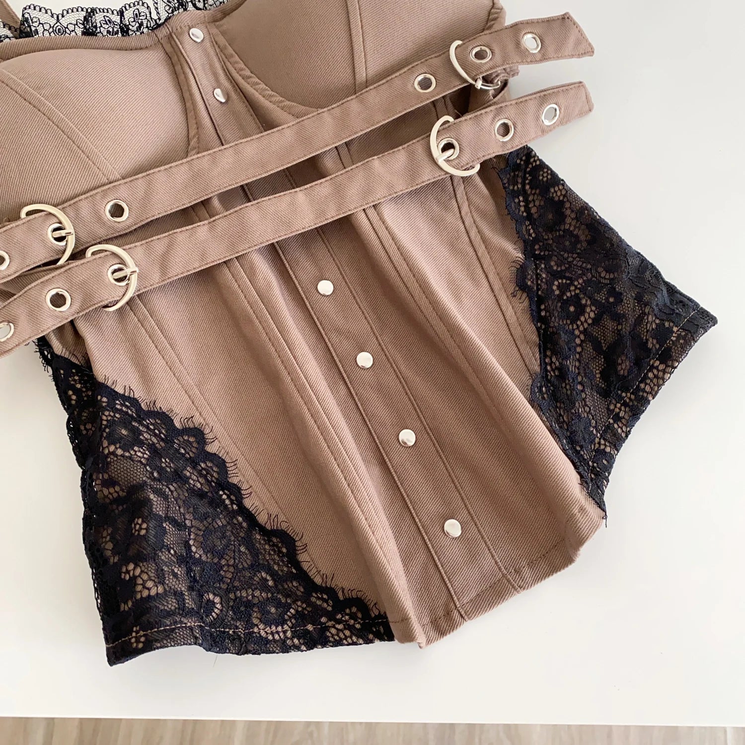 Brown garment with lace trim and metal buckles on a white background