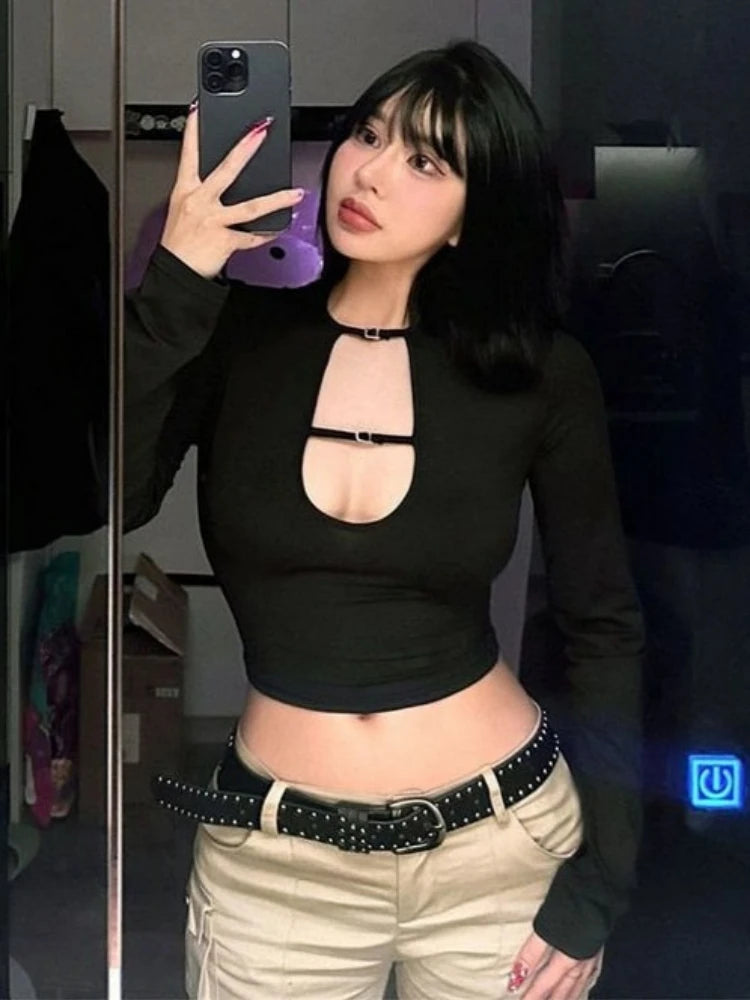 Person wearing a black long-sleeve top with cut-out design and beige pants, taking a mirror selfie.