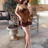 Woman in a brown dress taking a selfie in an indoor setting with plants and furniture.