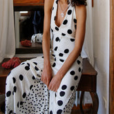Woman wearing a white dress with black polka dots sitting on a wooden bench.