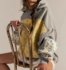 Person wearing a gray hoodie with floral patterns sitting on a chair.