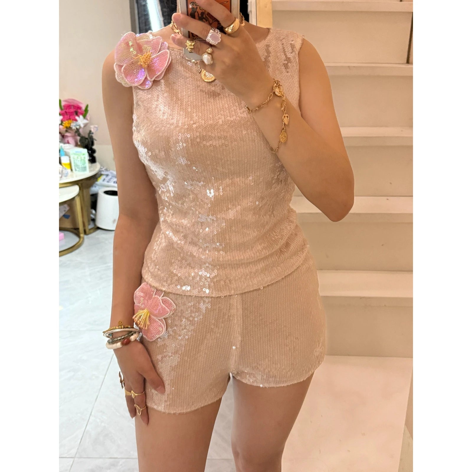 Person wearing a sequined top and shorts set with floral accessories indoors.
