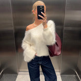 Person wearing a white fluffy sweater and dark jeans, holding a phone in an elevator.