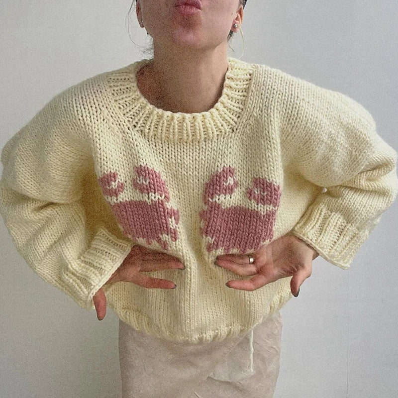 Person wearing a cream sweater with pink cat patterns on a plain background