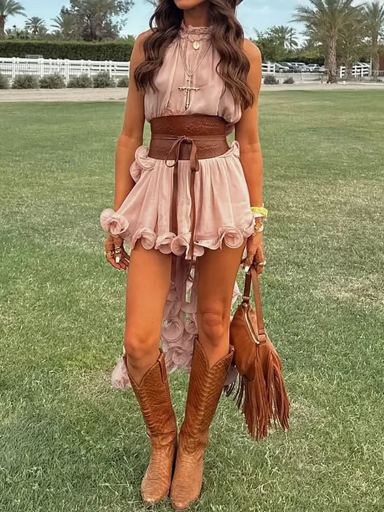 Woman in a pink dress with brown belt and boots standing on grass