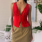 Person wearing a red sleeveless top with ruffles and beige pants on a porch.