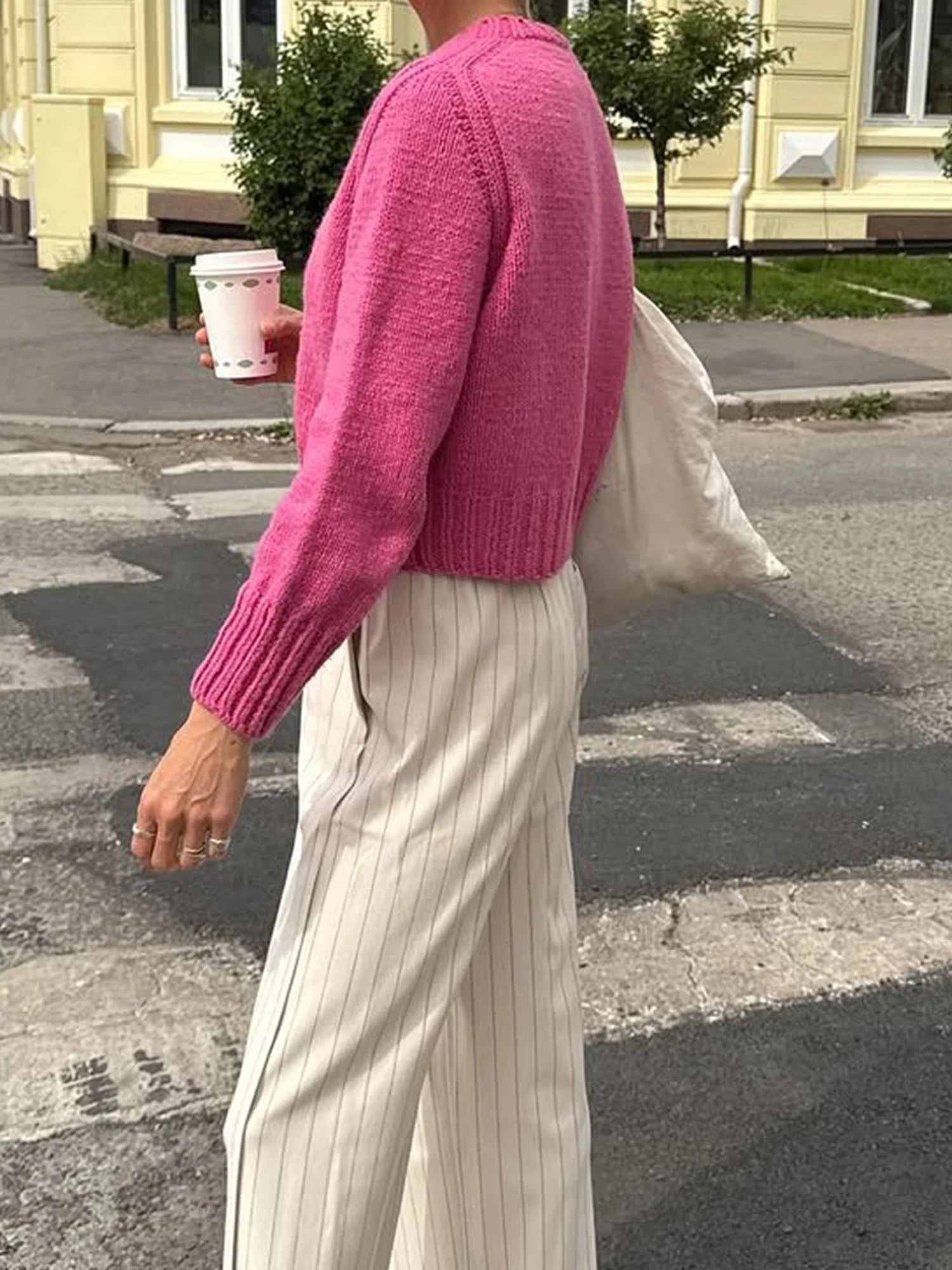 Person wearing a pink sweater and light-colored pants on a street.