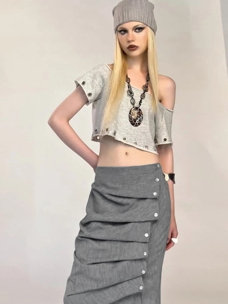 Person wearing a gray outfit with a long skirt and crop top on a plain background