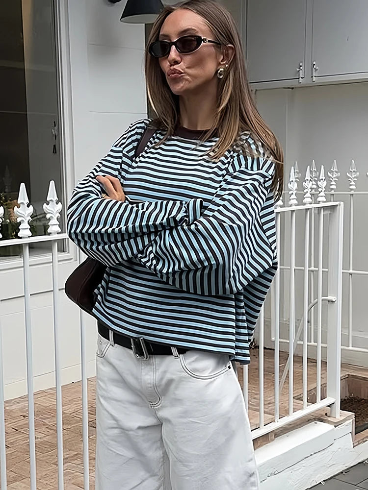 Person wearing a black and white striped sweater and white pants standing on a porch.