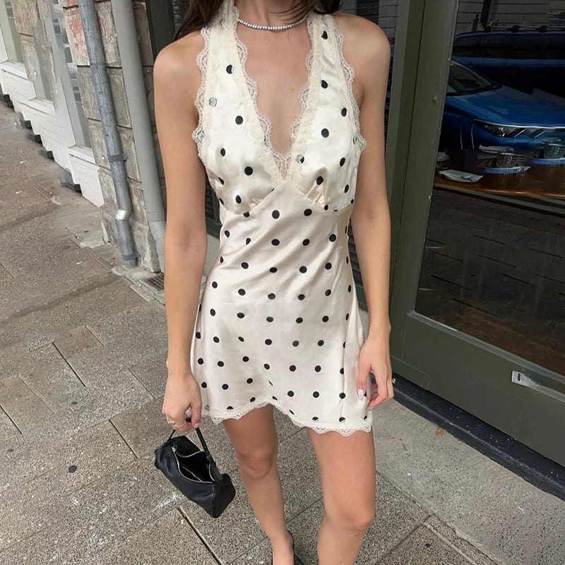 Woman wearing a white dress with black polka dots on a sidewalk.