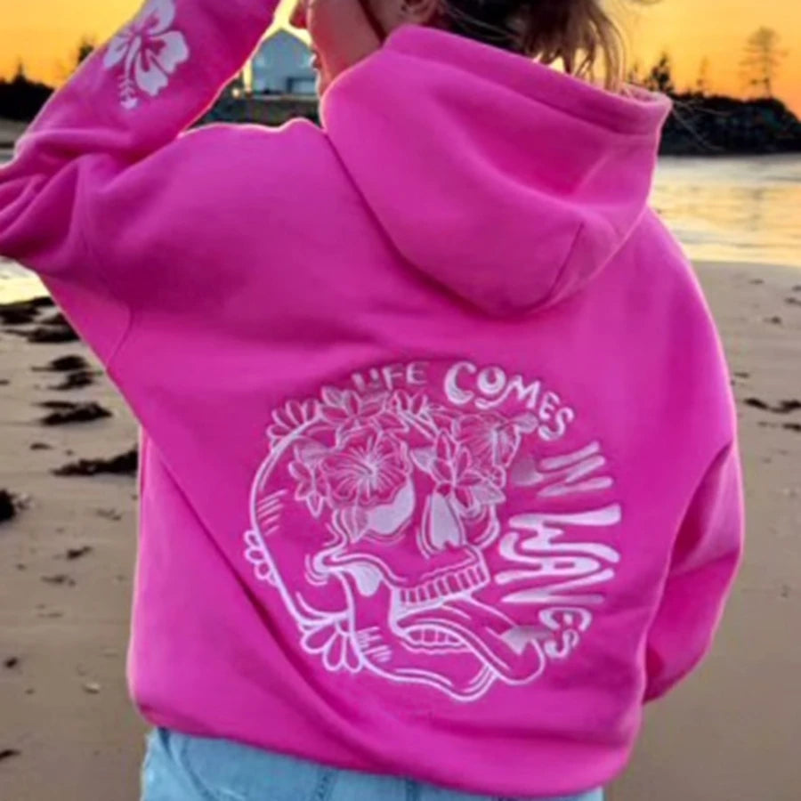 Person wearing a bright pink hoodie with a design and text on a beach.