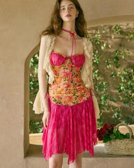 Woman wearing a floral top and pink skirt with a beige cardigan in an outdoor setting.