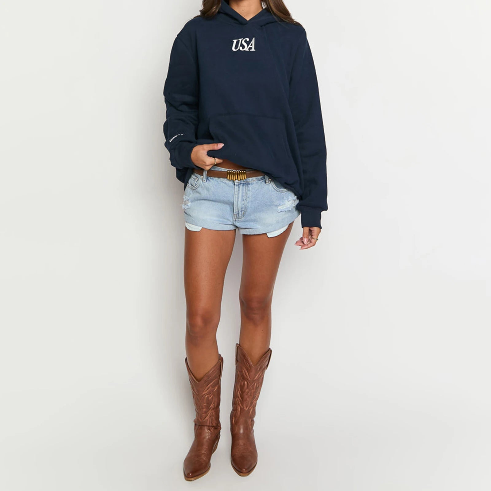 Person wearing a navy hoodie with 'USA' logo, light denim shorts, and brown cowboy boots