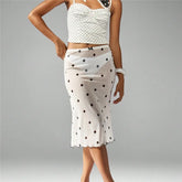 Woman wearing a white polka dot top and skirt on a gray background