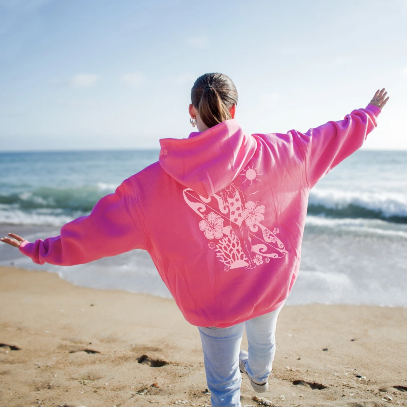 Person wearing a bright pink hoodie with a design on the beach