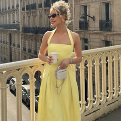 Woman in a yellow dress standing on a balcony holding a coffee cup.