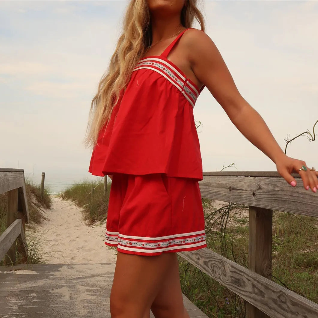 Woman in a red dress standing on a wooden path near a beach.
