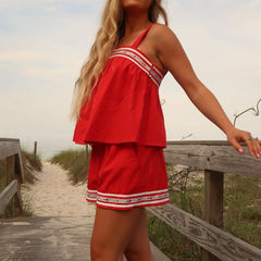 Woman in a red dress standing on a wooden path near a beach.