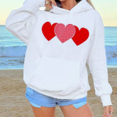 Person wearing a white hoodie with red heart designs on a beach