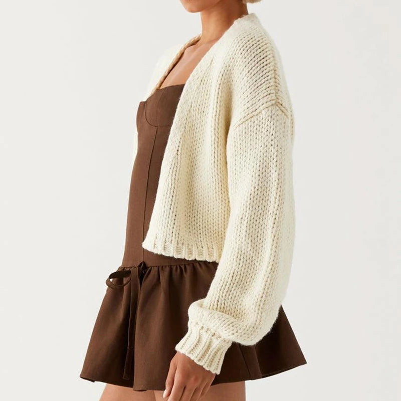 Person wearing a white knitted cardigan over a brown dress on a light gray background