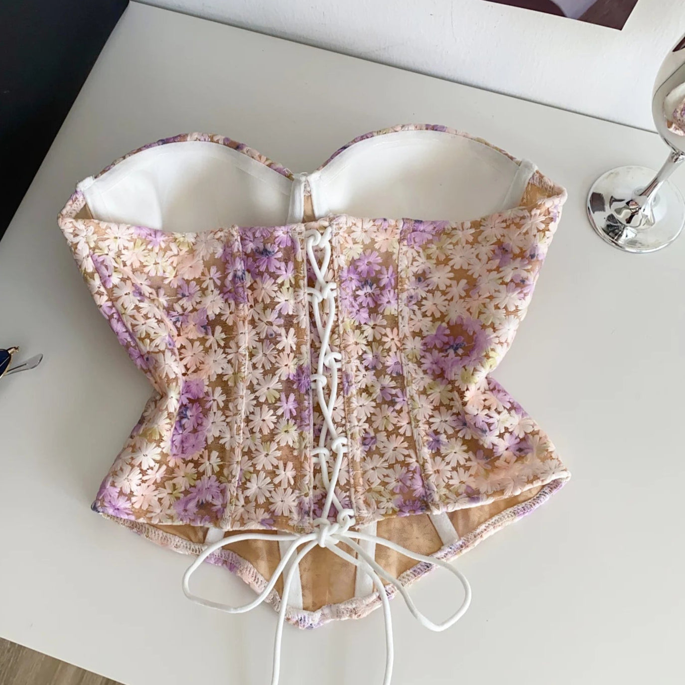 Floral-patterned corset on a white surface with a spoon and black object in the background.