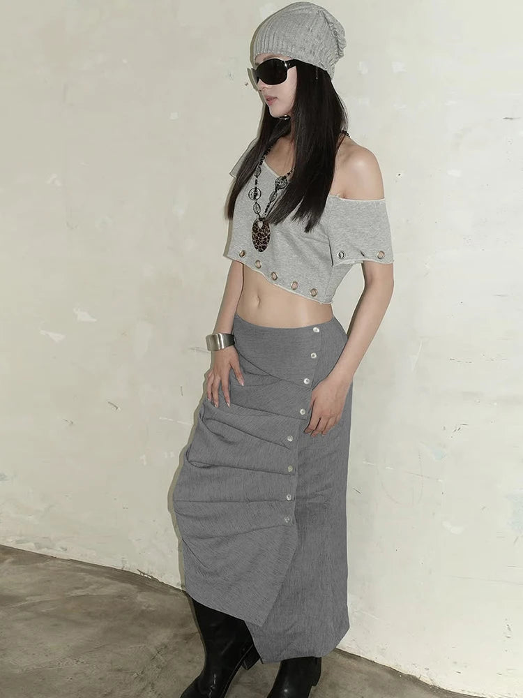 Person wearing a gray crop top and skirt with a white wall background