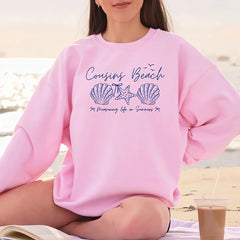 Person wearing a pink sweatshirt with 'Cousins Beach' text and graphics on a beach.